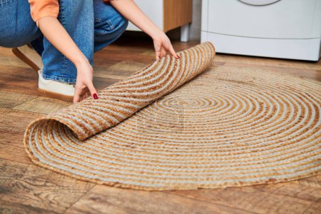 A woman kneels beside a rug, dressed casually, cleaning her home in a serene and purposeful manner.