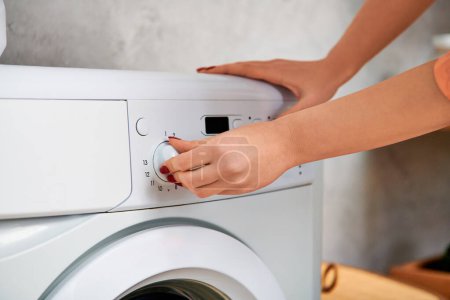 A stylish woman in casual attire carefully attaches a button onto a washing machine.