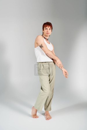 Téléchargez les photos : Un jeune homme élégant pose dans un studio sur fond gris, vêtu d'un débardeur blanc et d'un pantalon kaki. - en image libre de droit