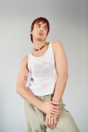 Téléchargez les photos : Un jeune homme élégant pose en studio, vêtu d'un débardeur blanc et d'un pantalon kaki sur fond gris. - en image libre de droit