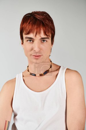 Photo for A stylish young man with red hair confidently poses in a white tank top against a grey studio backdrop. - Royalty Free Image