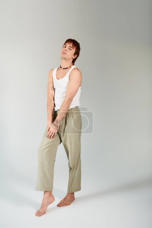 Téléchargez les photos : Un jeune homme élégant pose en studio sur fond gris, vêtu d'un débardeur blanc et d'un pantalon kaki. - en image libre de droit