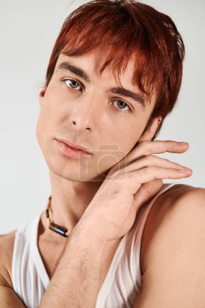 Un jeune homme élégant avec les cheveux roux frappant une pose dans un cadre studio avec un fond gris.