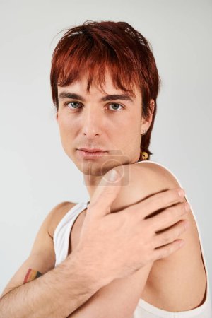 Foto de Un joven elegante con el pelo rojo posa con confianza en una camiseta blanca sobre un fondo gris de estudio. - Imagen libre de derechos