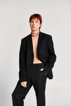A stylish young man in a suit striking a confident pose in a studio with a grey background.