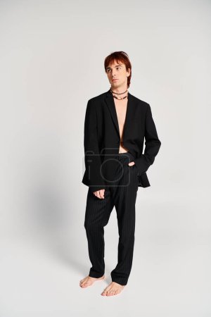 Ein stilvoller junger Mann im schwarzen Anzug steht selbstbewusst vor einem schlichten weißen Hintergrund in einem Studio-Setting..