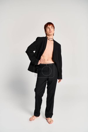 Ein stilvoller junger Mann im Anzug posiert selbstbewusst vor grauem Studiohintergrund.