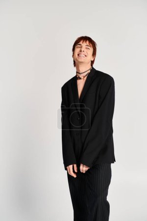 Photo for A stylish young man striking a pose in a black suit against a grey studio background. - Royalty Free Image