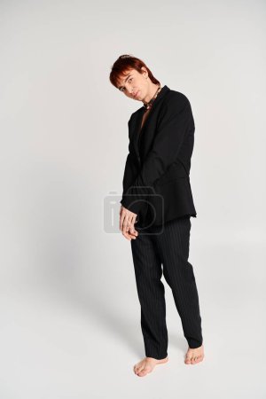 A stylish young man in a black suit striking a confident pose in front of a plain white background.