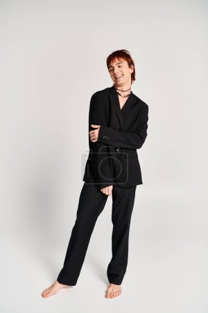 Foto de Un hombre sofisticado con un traje negro logra una pose cautivadora con confianza en un estudio sobre un fondo gris. - Imagen libre de derechos