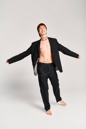 Un jeune homme élégant en costume prend une pose confiante dans un studio avec un fond gris.