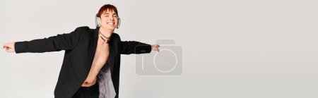 Photo for Young man in black jacket spreads his arms out in a dynamic pose against a grey studio background. - Royalty Free Image