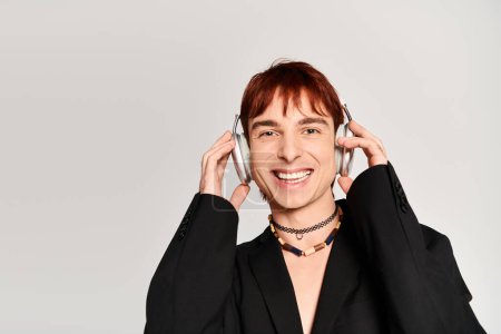 Téléchargez les photos : Un jeune homme élégant aux cheveux roux portant des écouteurs sur fond de studio gris. - en image libre de droit