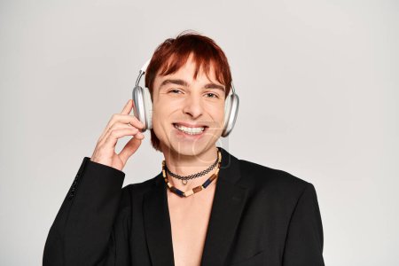 Téléchargez les photos : Un jeune homme élégant aux cheveux roux écoutant de la musique à travers des écouteurs dans un studio avec un fond gris. - en image libre de droit