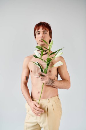 A shirtless young man gracefully cradles a plant in his hand, exuding a sense of peace and connection with nature.