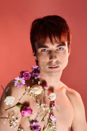 A shirtless man strikes a pose while holding flowers against a red background in a studio setting.