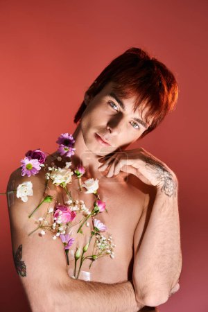 Foto de Un joven sin camisa se para en un estudio, sosteniendo con confianza un ramo de flores vibrantes contra el fondo. - Imagen libre de derechos
