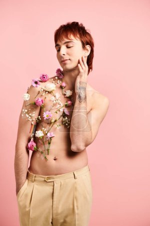 A shirtless young man strikes a pose with colorful flowers adorning his chest in a studio setting with a pink background