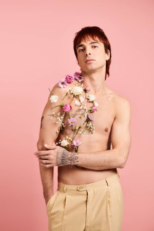 Foto de Un joven sin camisa sostiene con confianza un hermoso ramo de flores sobre un elegante fondo de estudio rosa. - Imagen libre de derechos