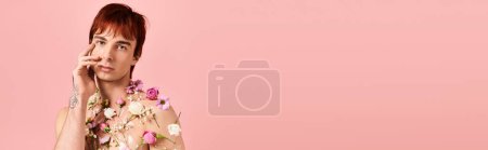 Foto de Un joven con estilo en una camisa con flores que tiene una conversación en un teléfono celular en un entorno de estudio con un fondo rosa. - Imagen libre de derechos