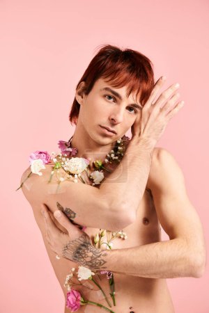 Téléchargez les photos : Un jeune homme torse nu pose avec des fleurs autour du cou sur un fond de studio rose. - en image libre de droit