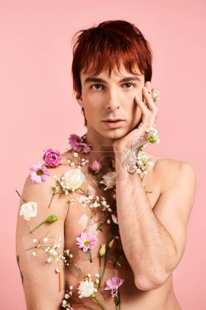 Foto de Un joven toma una pose con flores en el pecho contra un telón de fondo rosa en un estudio. - Imagen libre de derechos