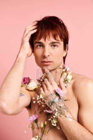 Un jeune homme pose torse nu dans un studio, guirlandes de fleurs drapées autour de son cou, sur un fond rose.