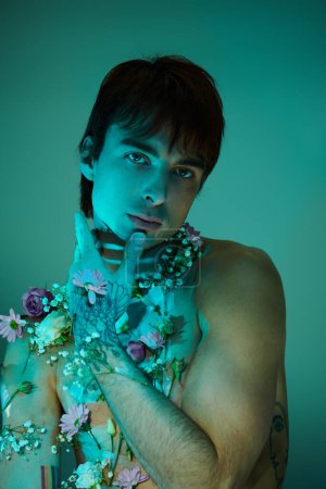 Téléchargez les photos : Un jeune homme se tient torse nu, orné de fleurs vibrantes, exsudant un sentiment de connexion avec la nature. - en image libre de droit