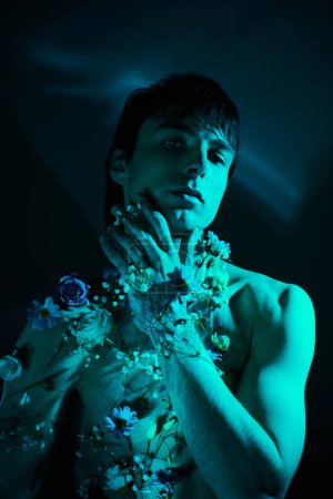 A shirtless man stands holding an array of vibrant flowers in his hands