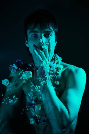 A shirtless young man holds colorful flowers in his hands against a blue light