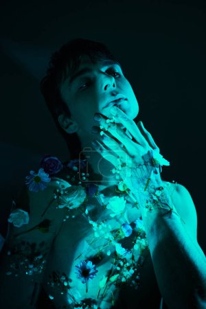 Foto de Un joven con las manos en la boca, rodeado de flores, con luz azul - Imagen libre de derechos