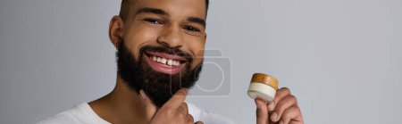 Téléchargez les photos : Un bel homme avec une barbe tenant un récipient de crème. - en image libre de droit