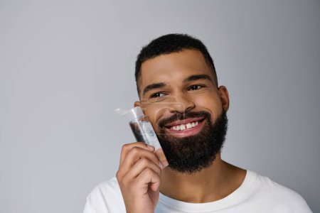 Photo for African american appealing man with a beard applying locion on his face. - Royalty Free Image