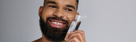 Hombre guapo afroamericano con barba aplicándose loción en la cara.