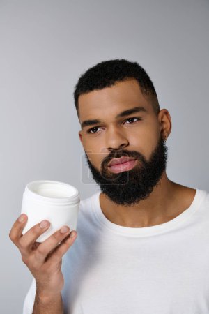 Photo for African american appealing man with a beard holding jar of cream. - Royalty Free Image