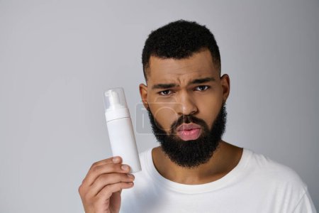 Guapo joven afroamericano con barba sosteniendo un tubo de loción.
