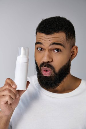 Téléchargez les photos : Appel jeune homme afro-américain avec une barbe tenant un tube de locion. - en image libre de droit