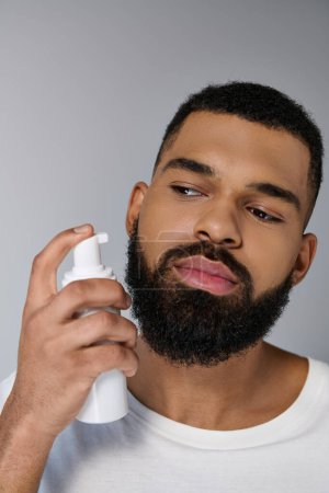 Séduisant jeune homme afro-américain avec une barbe tenant un tube de locion.