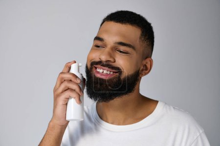 Hombre afroamericano joven y guapo con barba sosteniendo un tubo de loción.
