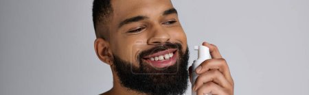 Joven afroamericano con barba sosteniendo un tubo de loción.