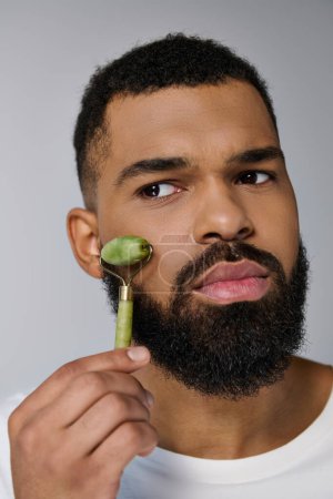Photo for Bearded man holds face roller for skincare routine. - Royalty Free Image