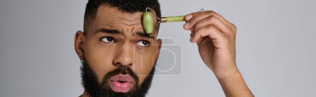 African american stylish man holds face roller for skincare routine.