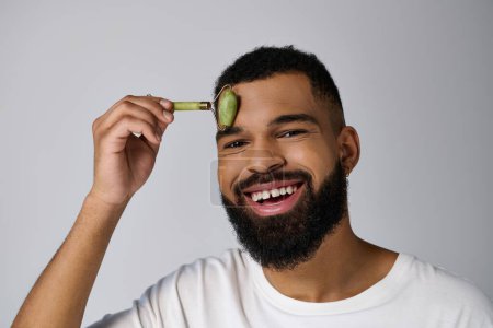 African american young man holds face roller for skincare routine.