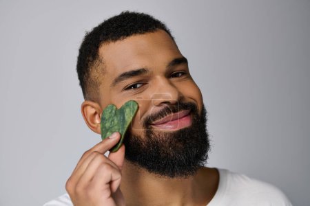African american young man holds gua sha for skincare routine.