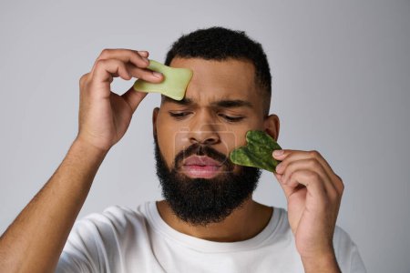 African american handsome man holds gua sha for skincare routine.