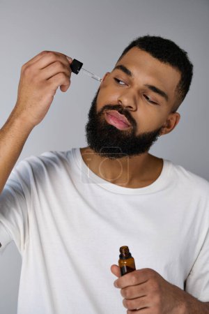 A handsome young man with a beard holding a bottle of essential oils.