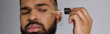 African american stylish man with a beard holding a bottle of serum.