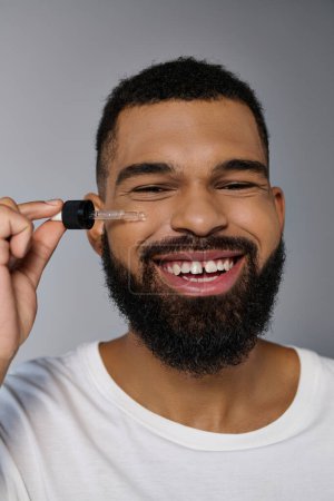 Téléchargez les photos : Afro-américain attrayant jeune homme avec une barbe tenant une bouteille de sérum. - en image libre de droit