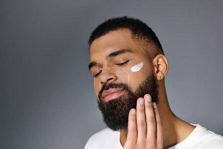 Téléchargez les photos : Jeune homme afro-américain avec une barbe présentant de la crème blanche sur son visage. - en image libre de droit