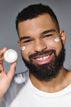 Photo for Handsome young man with a beard holding a jar of cream. - Royalty Free Image